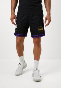 Čierne basketbalové šortky s fialovými lemami a žltým logom "Lakers", vyrobené z priedušného materiálu, v kombinácii s bielymi športovými topánkami a ponožkami.