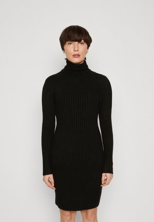 Zwarte geribbelde tricot jurk met hoge col en lange mouwen, aansluitende silhoutte en knielange zoom, weergegeven tegen een neutrale achtergrond.