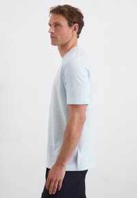  Lichtblauwe t-shirt met korte mouwen en ronde hals, gemaakt van een zachte stof. Heeft een subtiele textuur en zijsplitjes aan de zoom.