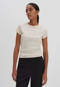 Light beige ribbed T-shirt with a crew neckline and short sleeves, paired with black trousers. Smooth texture, fitted design.