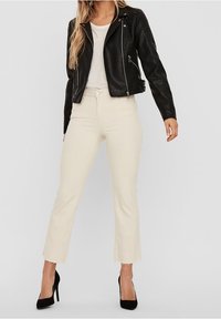 Giacca in pelle nera da motociclista con cerniere, t-shirt bianca, jeans cropped crema e scarpe nere con tacco alto.