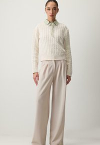 Valkoinen neulepaita, jossa on vaaleanvihreä kaulus ja nauhatyylitys, yhdistettynä leveälahkeisiin, vaaleanbeigeihin housuihin. Pehmeä rakenne ja rento istuvuus.