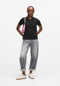 Fekete poloing gombos gallérral, felgöngyölt szürke farmernadrággal és fehér sportcipővel párosítva. Kiegészítve egy kis rózsaszín kézitáskával.