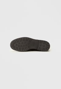 Semelle extérieure en caoutchouc noir avec un motif de semelle robuste comportant des triangles et des rainures pour une meilleure traction. Bords lisses et conception solide et durable.
