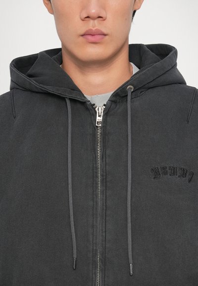 Čierna mikina na zips s textúrovaným povrchom, sťahovacími šnúrkami a vyšívaným logom na hrudi, s voľným, ležérnym strihom.