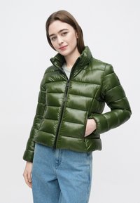 Metallic grøn pufferjakke med høj krave og lynlåslukning. Har vandret quiltet polstring, sidelommer og sorte hardware-detaljer.