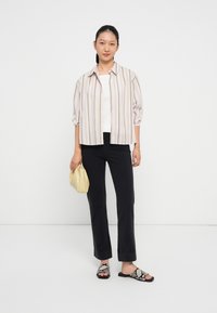 Camisa de botão às riscas em cores claras, calças pretas, sandálias de estampado de cobra e uma pequena mala de ombro amarela. Texturas suaves e ajuste descontraído.