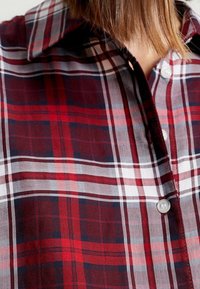 Rød og marineblå ternet skjorte med krave, der har knaplukninger og en blød stoftekstur. Fremtrædende horisontale og vertikale striber.