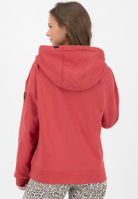 Felpa rossa con un ampio cappuccio, polsini e orlo a coste. Presenta un logo sul lato ed è abbinata a pantaloni con stampa leopardata.