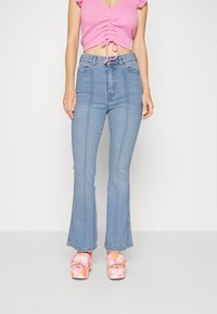 Helle blå højtaljede flared jeans med frontseams; parret med en lyserød ribbet cropped top og blomster platformhæle.
