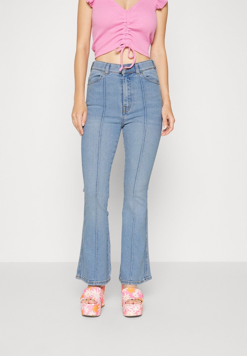 Helle blå højtaljede flared jeans med frontseams; parret med en lyserød ribbet cropped top og blomster platformhæle.