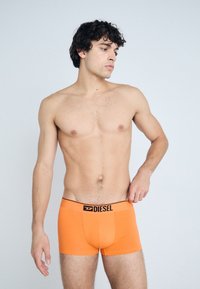 Boxers oranges avec un logo Diesel noir sur la ceinture, fabriqués en tissu extensible, coupe ajustée et texture lisse.