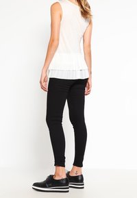 Bílý top bez rukávů s plisovaným lemem, spárovaný s černými skinny džíny a černými platformovými botami s bílou pruhovanou podrážkou.