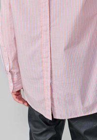 Light pink striped shirt with thin blue lines, buttoned cuffs, and a slightly relaxed fit. Back view displaying vertical seams. Black pants visible.