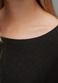 Musta, kevyt paita pyöreällä kaula-aukolla ja hienovaraisella pinnalla, joka tarjoaa sileän kankaan laskeutumisen solisluiden ympärille.