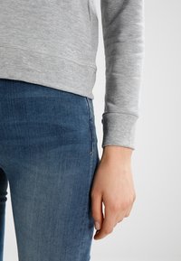 Harmaa puuvillainen svetaritakki resorihihoilla, yhdessä sinisten farkkujen kanssa, joissa on hieman haalistunut väri ja etutaskun yksityiskohta.