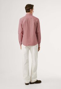 Rot-weißer Karoflanell mit langen Ärmeln und Button-Down-Kragen, mit einem abgerundeten Saum, getragen mit weißen Hosen und braunen Schuhen.