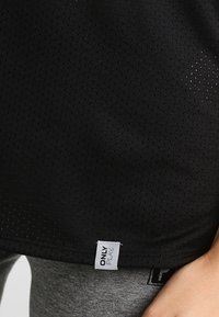 Black mesh sports top with white "ONLY PLAY" label above gray leggings, showing close-up of lower torso and hand resting by side.