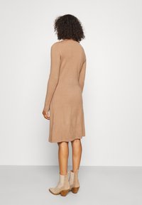 Abito a maglia in una tonalità beige, aderente al corpo con gonna svasata, maniche lunghe, abbinato a stivaletti alla caviglia beige chiaro.
