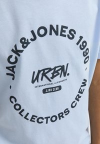 Camiseta de algodón azul claro con un gráfico circular que presenta un texto en negro en negrita: "JACK & JONES 1990", "URBN" y "COLLECTORS CREW".