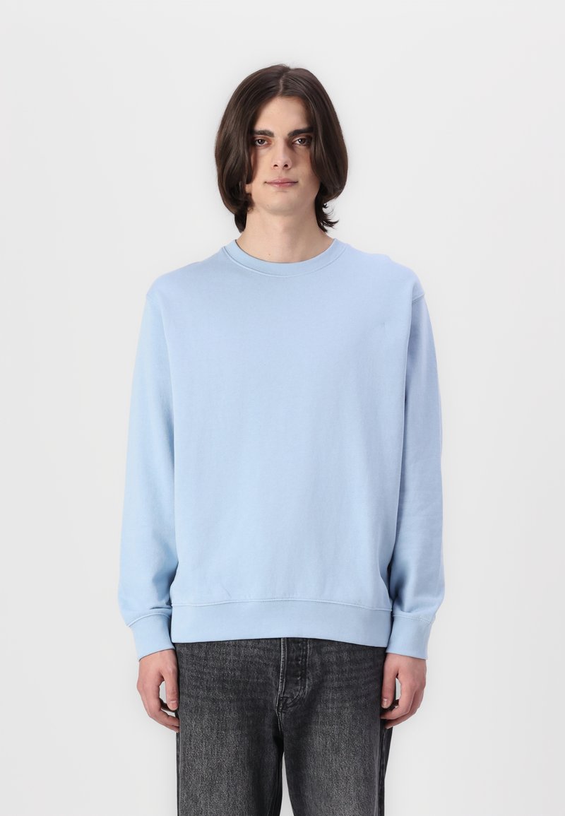 Lichtblauwe crewneck sweatshirt van zachte stof, met lange mouwen, geribde manchetten en een ontspannen pasvorm, gecombineerd met Donkergrijze jeans.
