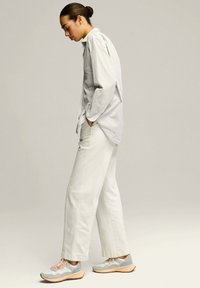 Camisa blanca a rayas con botones, pantalones blancos sueltos y zapatillas grises con cordones rosa y suelas beige. Diseño simple y moderno.