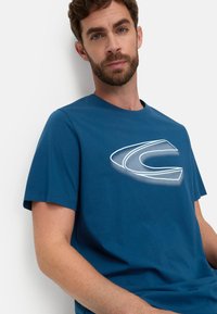 Blue cotton t-shirt featuring a large white graphic logo on the front. Short sleeves and a round neckline with a soft texture.