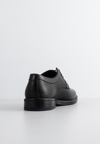 Chaussure habillée en cuir noir avec panneau en maille texturé, bout rond, design à lacets et talon lisse. Caractérisée par une semelle noire à profil bas.