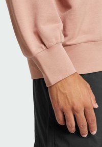 Sweatshirt rosa chiaro in tessuto testurizzato, con maniche arricciate e polsini aderenti. Abbinato a pantaloni corti scuri, che enfatizzano il contrasto di colore.