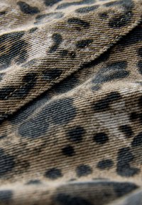 Nahaufnahme eines beigen Stoffs mit schwarzem Leopardenmuster und sichtbarer diagonaler Naht.