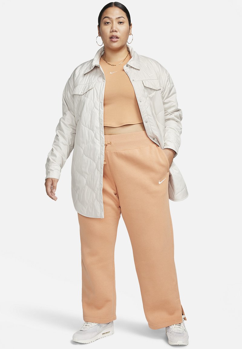 Veste matelassée gris clair sur un débardeur pêche, associée à un pantalon de survêtement pêche avec des fentes sur les côtés et des accents blancs de Nike. Des sneakers blanches complètent le look.