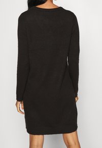 Robe pull en tricot marron foncé avec manches longues, col rond, fentes sur les côtés, texture douce et détails en côtes au niveau de l'ourlet.