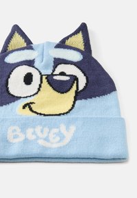 Pletená čepice s designem kreslené lišky v modré a námořnické barvě. Čepice má ohnutý lem a vyčnívající uši, s nápisem "Bluey" v bílém.