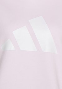 Bílý trojpruh Adidas na světle růžové tkanině, připomínající stylizovaný trojúhelník s zaoblenými hranami.