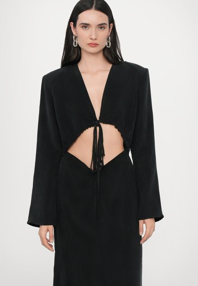 Robe noire avec un décolleté plongeant et des manches longues. Présente une découpe à la taille et un accent noué au centre. Texture douce.