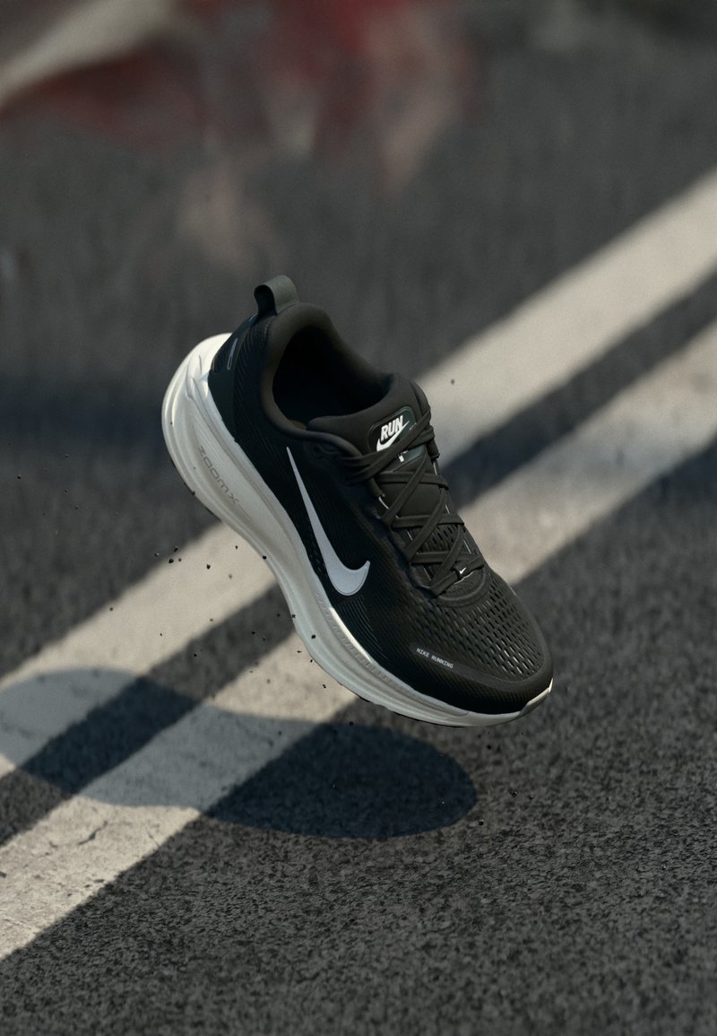 Chaussure de course noire et blanche en plein air au-dessus d'une route asphaltée avec une ligne blanche, montrant les logos « RUN » et Nike swoosh.