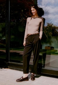 Light beige long-sleeve top, high-waisted black trousers with a braided belt, and dark brown loafers with a textured surface, standing outdoors.