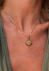 Gold necklace with a sunburst pendant featuring a central eye design. The chain has elongated, flat links.