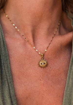 Gold necklace with a sunburst pendant featuring a central eye design. The chain has elongated, flat links.
