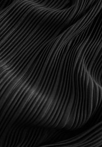 Černá skládaná tkanina s vertikálními žebry, která ukazuje hladkou texturu a plynulý vzhled, vytvářející hloubku a rozměr.