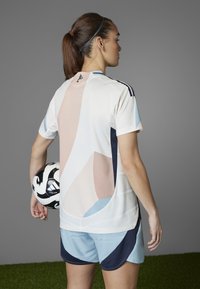 Camiseta deportiva con formas abstractas en rosa, azul y blanco. Incluye pantalones cortos azul oscuro y un balón de fútbol blanco y negro.