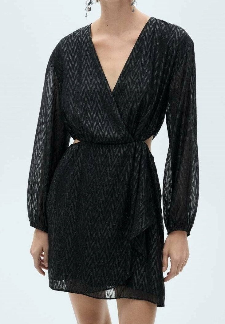 Czarna, długorękawowa mini sukienka w zygzakowy wzór, z głębokim dekoltem w kształcie V, wyciętymi bokami i sukienką w stylu kopertowym na stojącej osobie.