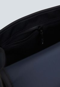 Interno di una borsa nera che mostra una texture liscia, con una tasca con zip e un compartimento in rete, evidenziando elementi di design funzionali.