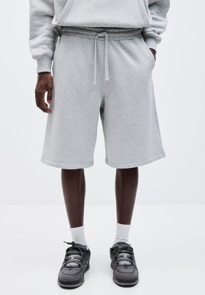 Shorts en coton gris avec une taille élastique et un cordon de serrage, dotés de poches latérales et d'une coupe décontractée, accompagnés de chaussures noires.