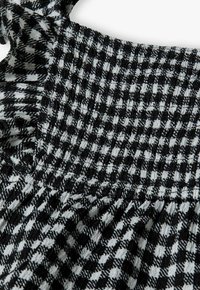 Haut en tissu smocké avec un motif à carreaux noir et blanc. Bords volantés avec une finition texturée et une silhouette structurée.