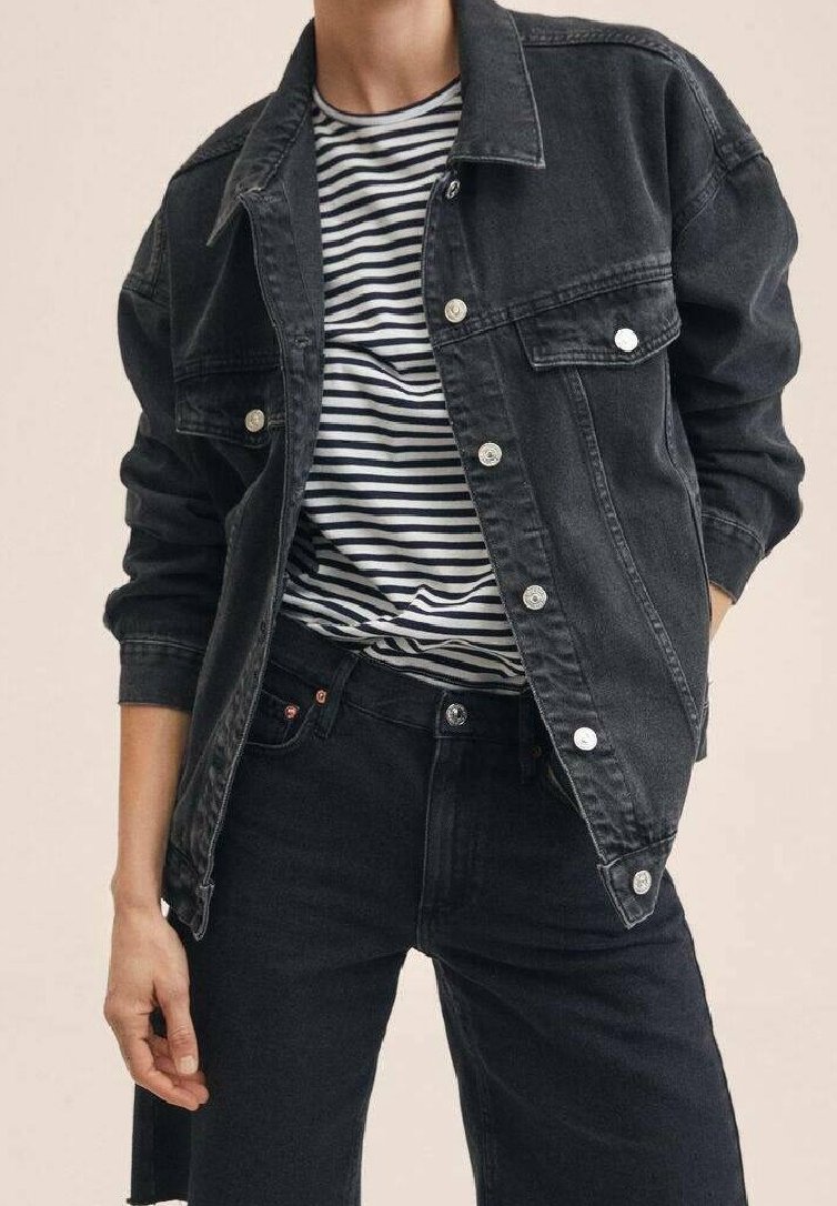 Giacca in denim nera con due tasche frontali, bottoni silver e maniche arrotolate, abbinata a una t-shirt in cotone a righe e jeans neri.