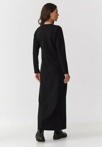 Czarna, długo rękawowa sukienka maxi o prostym kroju, z okrągłym dekoltem i rozcięciem z tyłu dla swobody ruchów. Gładki, gęsty materiał i minimalistyczny design.