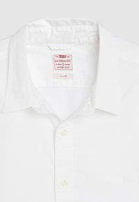 Slim-fit bela srajca s kragnico, izdelana iz bombaža, z Levi's oznako in oznako 'Battery Shirt' ter gumbnim zapiranjem. Gladko teksturo.
