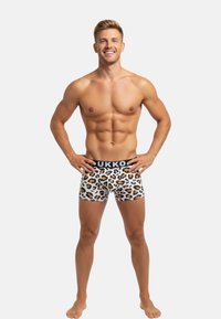 Boxershorts aus einem weißen Stoff mit einem Leopardenmuster in Braun und Schwarz. Sie verfügen über einen schwarzen Bund mit dem Markennamen "UKKO."