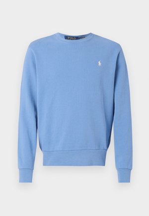 Zils džemperis ar apaļu kakla izgriezumu, izgatavots no mīkstas auduma, ar ribotām piedurknēm un apakšmalu, ar nelielu baltu logotipu uz krūtīm.